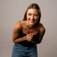 Thumbnail for Smiling young woman wearing a black top and blue jeans, exuding joy and happiness.