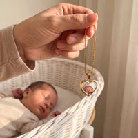 Thumbnail for The gold heart photo pendant held above a sleeping newborn, showing its real small size | SKU: TPH-CHTN-GOLD-SMALL